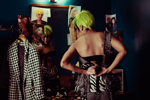Back view of trendy actress in bright wig reflecting in mirror while preparing for performance in makeup room