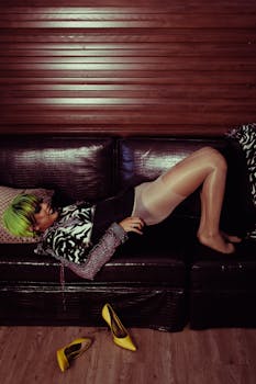 Side view of content stylish female in wig putting on nylon tights while lying on leather sofa in room