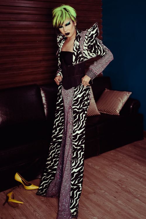 Free Young ethnic female theater artist with makeup in wig putting on ornamental trousers on parquet in dressing room Stock Photo