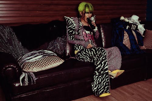 Extravagant Asian artist in costume drinking water on sofa