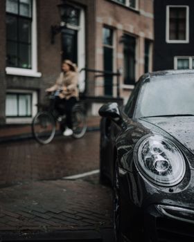 一辆黑色的豪华车停在街上，雨滴落下，一个女人骑着自行车经过，展现了城市的生活方式