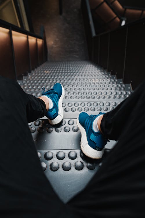 Person in Black Pants Wearing Blue Sneaker Sitting on a Metal Stairs