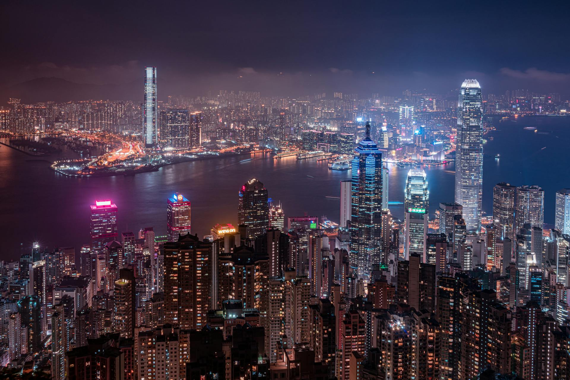 High-angle view of Hong Kong skyline at night, featuring iconic skyscrapers and vibrant lights.