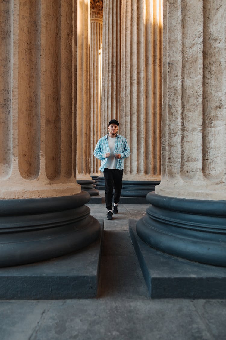 A Man In Blue Long Sleeves Walking Beside The Concrete Pillars