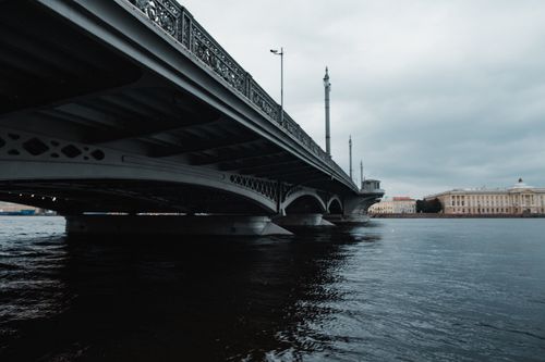 Free A majestic steel bridge spans a tranquil river with historic buildings in the background. Stock Photo