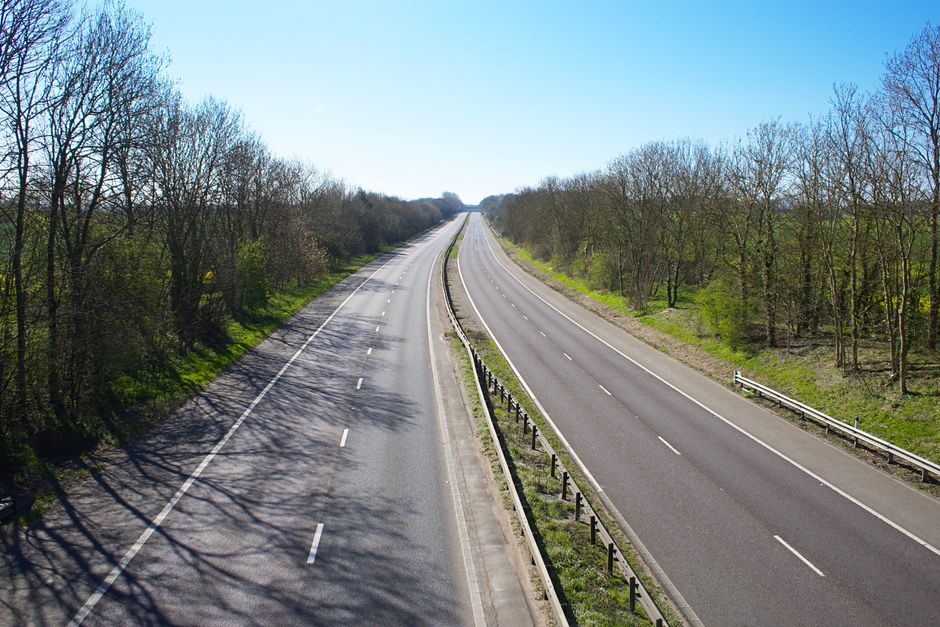 A peaceful view of an empty dual carriageway surrounded by leafless trees in rural UK.