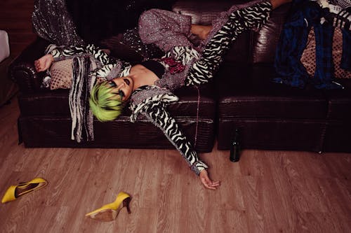 Tired transsexual man with bright hairstyle and makeup in fashionable clothes resting on leather sofa after party