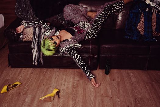 Tired transsexual man with bright hairstyle and makeup in fashionable clothes resting on leather sofa after party