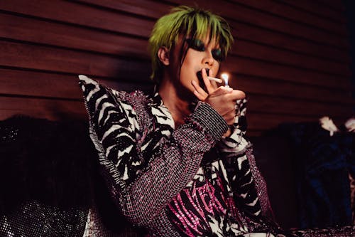 Thoughtful transgender model in stylish outfit smoking cigarette