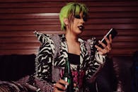 一位绿发时尚人士在室内使用智能手机，展现出大胆的风格