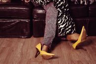 Crop unrecognizable crossdresser in stylish clothes taking off shoes while resting on comfortable couch