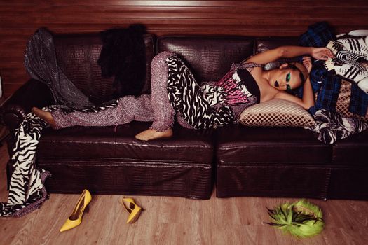 Full length of stylish female in bright outfit with makeup relaxing on comfortable leather couch after performance