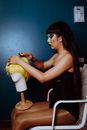 Side view of young male crossdresser with long straight hair and makeup in black bodysuit refining hairpiece for performance while sitting in chair