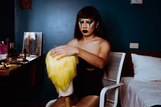Young male performer with dark hair and makeup combing yellow hairpiece while preparing for show in dressing room