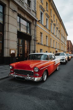 Classic red vintage car parked along a city street. Urban architecture backdrop.