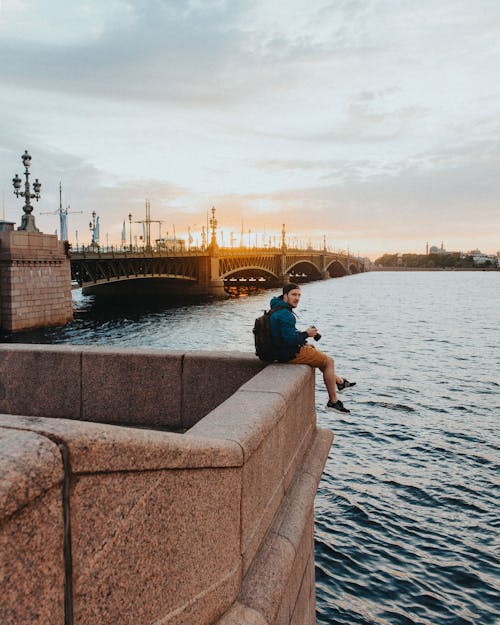 Free Man in Blue T-shirt Sitting on Concrete Dock Stock Photo