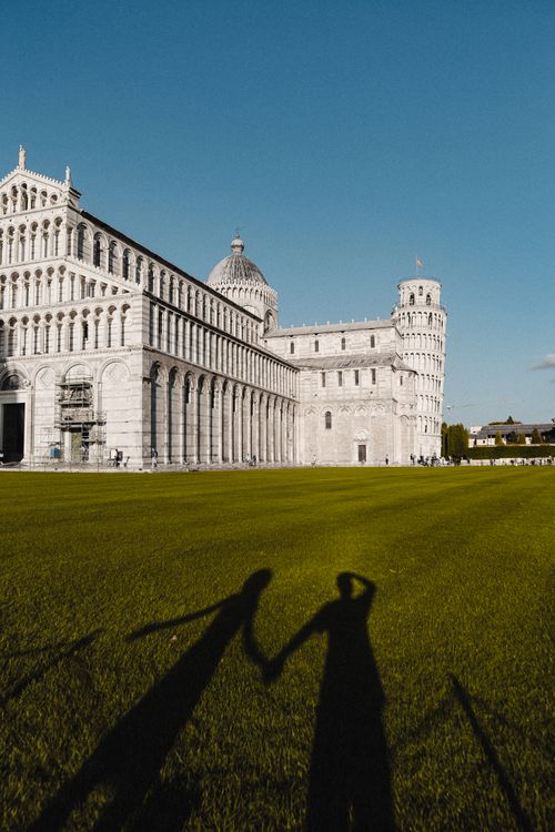 Free Shadows of a couple holding hands near the iconic Leaning Tower of Pisa under the blue sky. Stock Photo