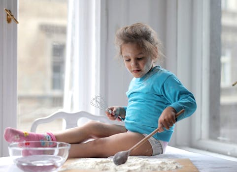 Child sitting by a window baking with flour, enjoying a playtime cooking moment indoors.