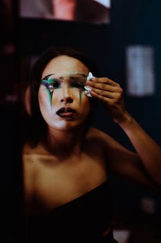 A young adult adjusting dramatic makeup in a mirror, capturing a thoughtful and creative moment.