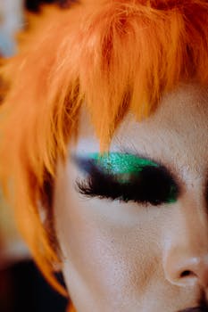 Vibrant close-up of androgynous model with orange wig and bold makeup. Studio shot.
