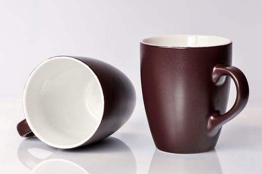 Two matte dark plum mugs with white interiors, one lying sideways