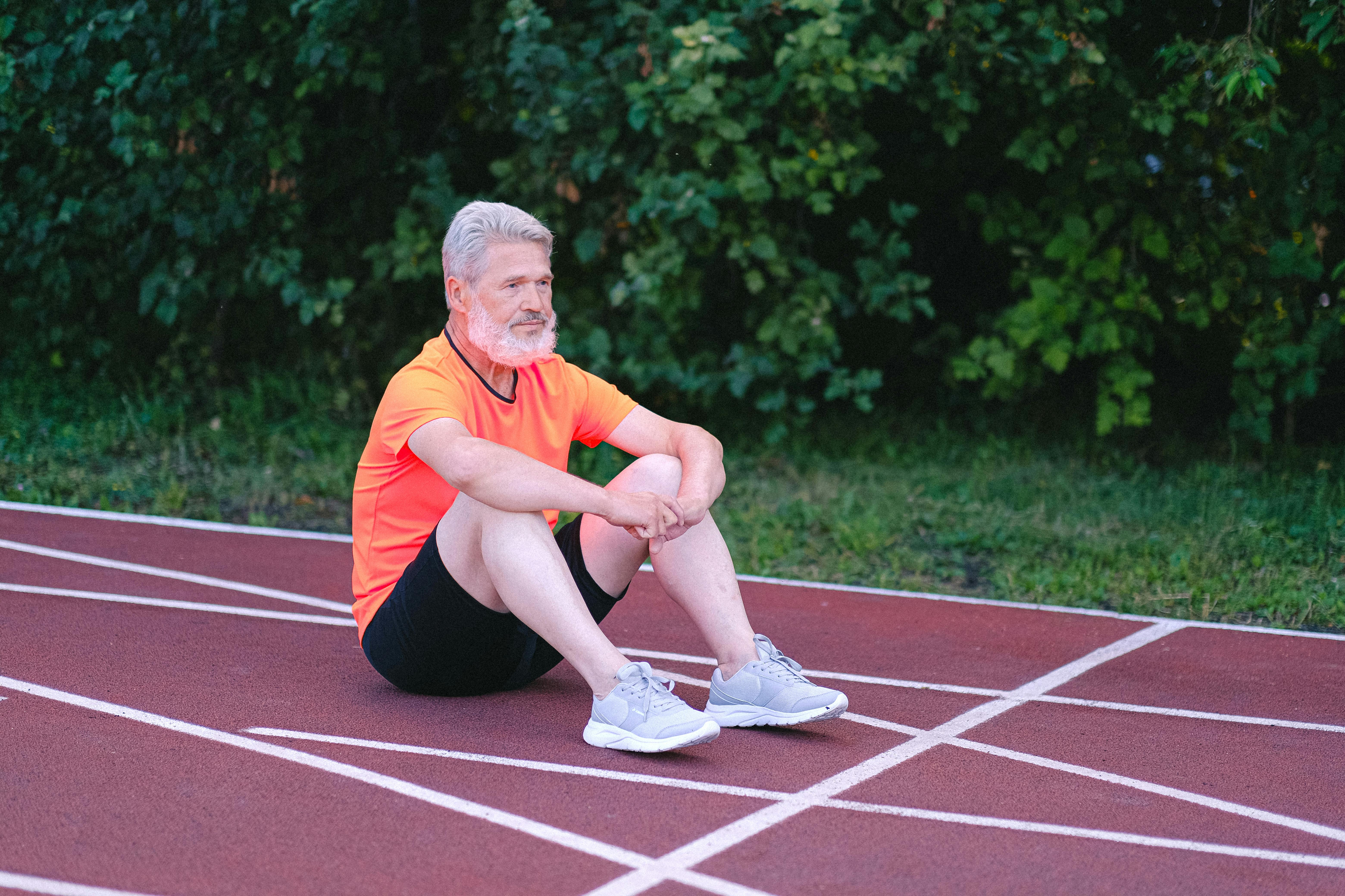 Senior man in activewear sitting on a track, reflecting. Outdoor fitness lifestyle.