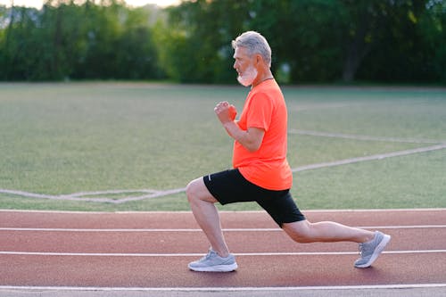 Free Side view of bearded male training and doing lunges on track on blurred background of greenery Stock Photo