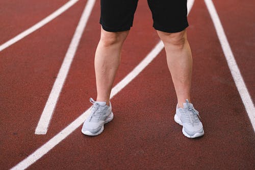 Crop anonymous sporty male in activewear practicing on racetrack of stadium in summer