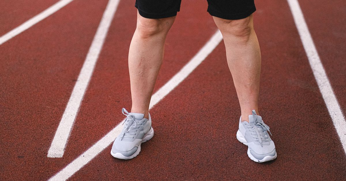 Crop anonymous sporty male in activewear practicing on racetrack of stadium in summer
