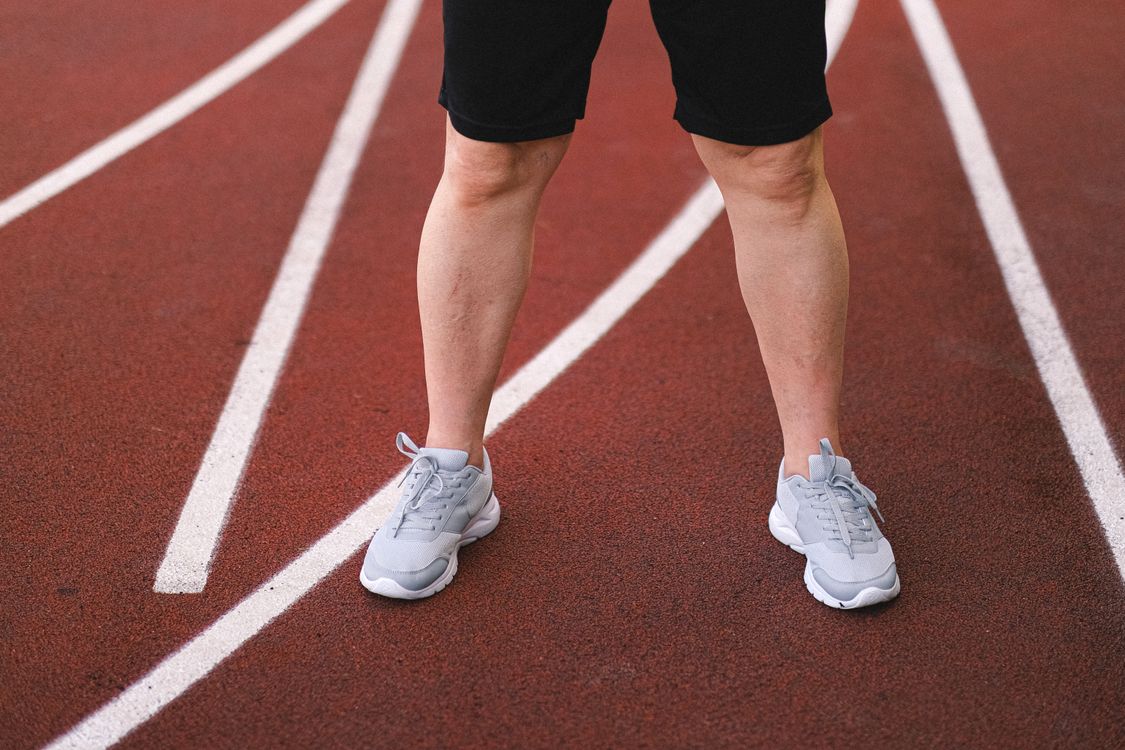 Person in Black Shorts and White Nike Sneakers Standing on Brown Field