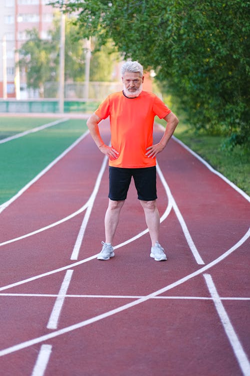 Full body of elderly male standing on track and preparing for running in daylight in summer