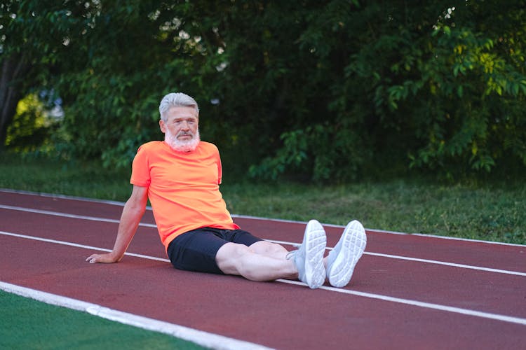 Senior Sportsman Resting On Racetrack With Green Bushes