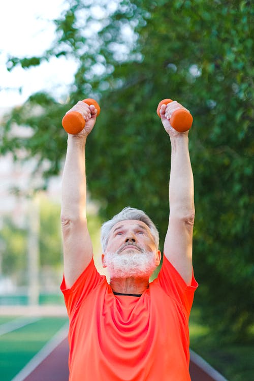 Free Senior man in sportswear doing exercises with dumbbells on stadium in sunny day Stock Photo