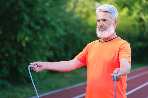 Focused elderly man with bread in sportswear standing wit jump rope on stadium and looking forward