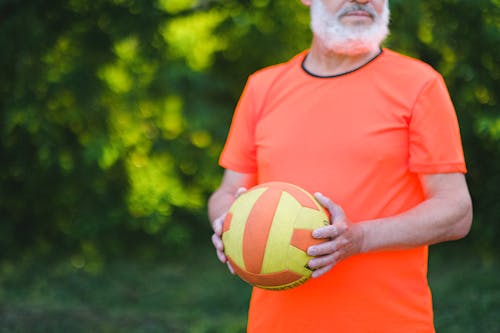 Crop unrecognizable senior man in sportswear holding ball during workout on street in daytime