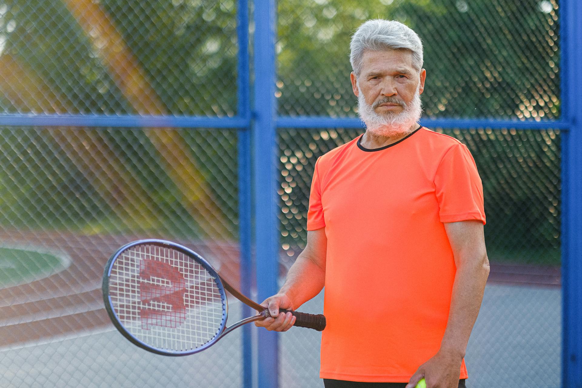 Focused senior sportsman in sportswear standing with racket while playing tennis on sports ground in sunny day