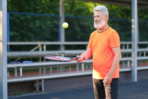 Cheerful aged sportsman playing tennis on tennis court