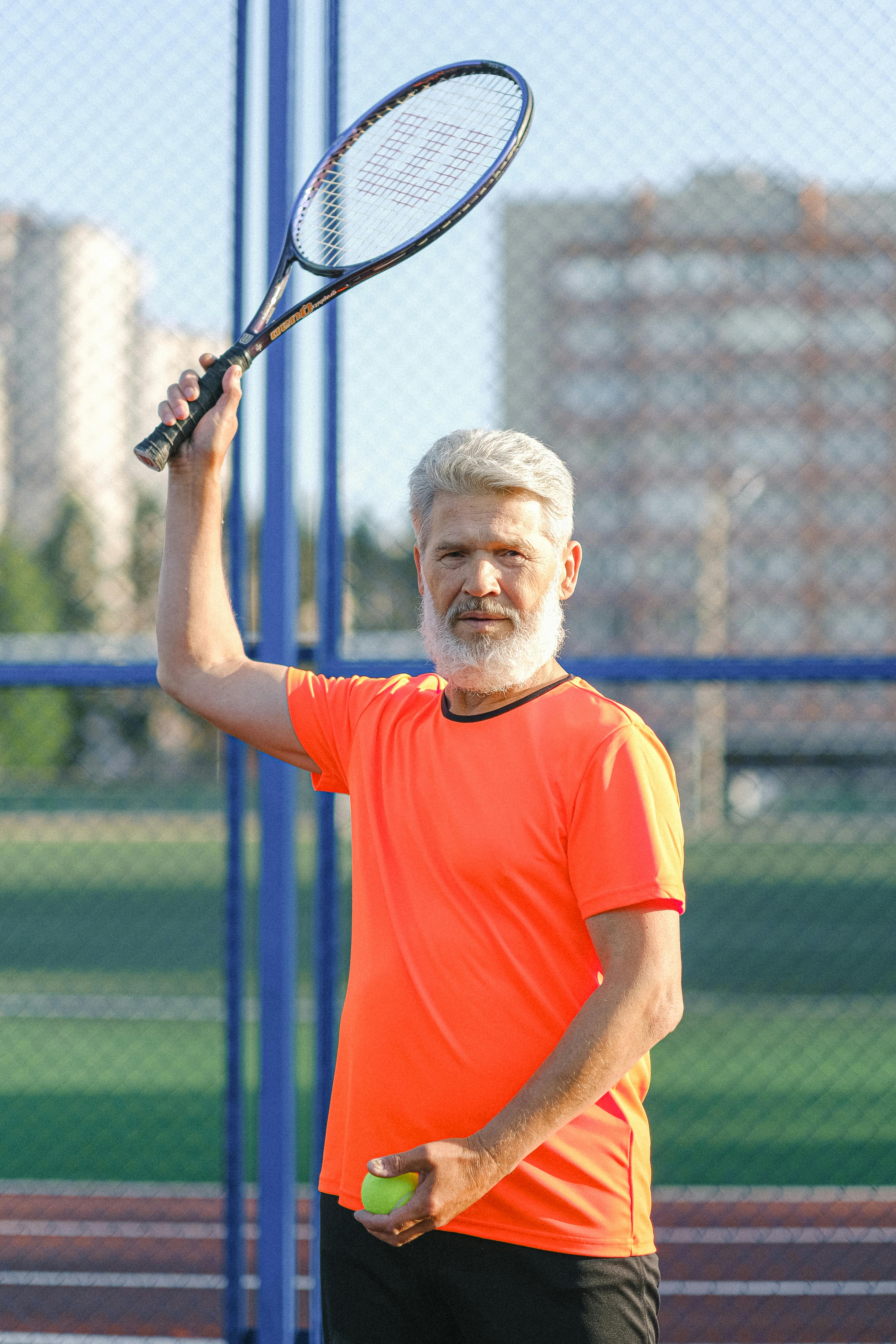 serious elderly sportsman raising hand with racket while playing tennis