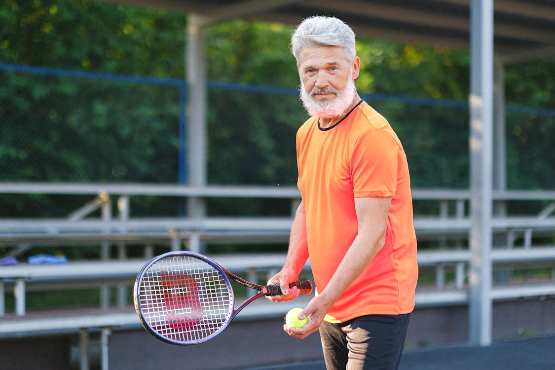 Free Positive senior sportsman in bright t shirt preparing to hit ball during tennis training on court in sunny day Stock Photo