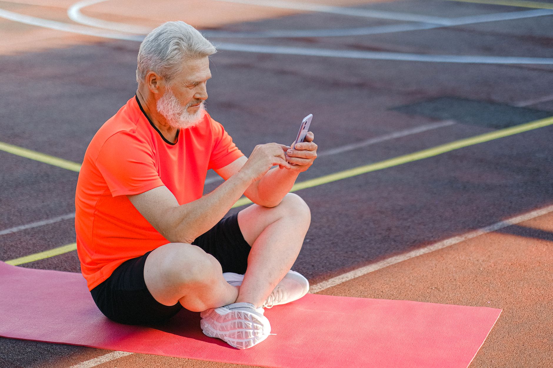 어르신 스마트폰 무료 교육 3 Full body of focused senior male athlete in sportswear sitting on stadium and browsing mobile phone during training