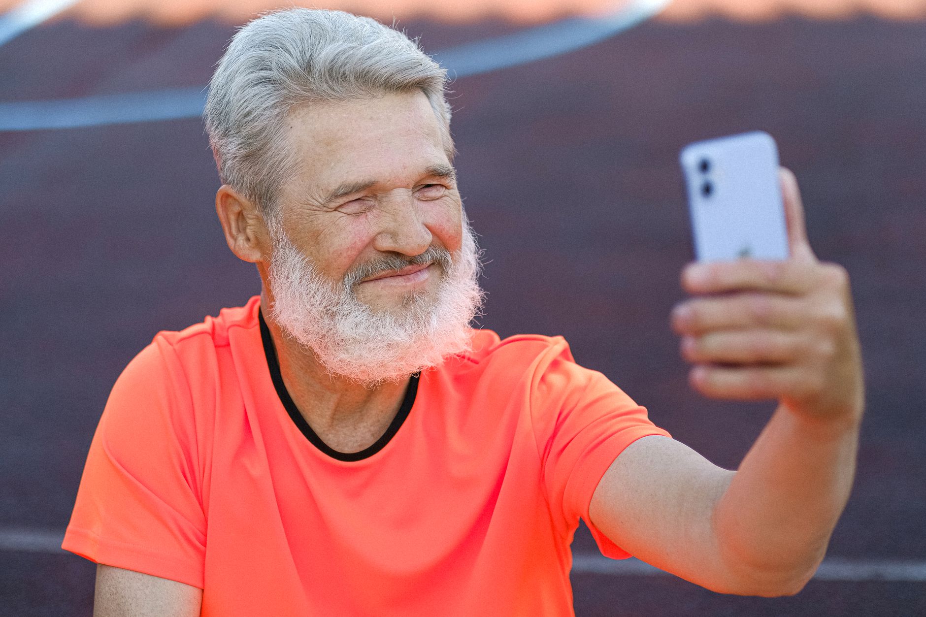 Happy elderly man with white hair taking a selfie on a smartphone while outdoors.