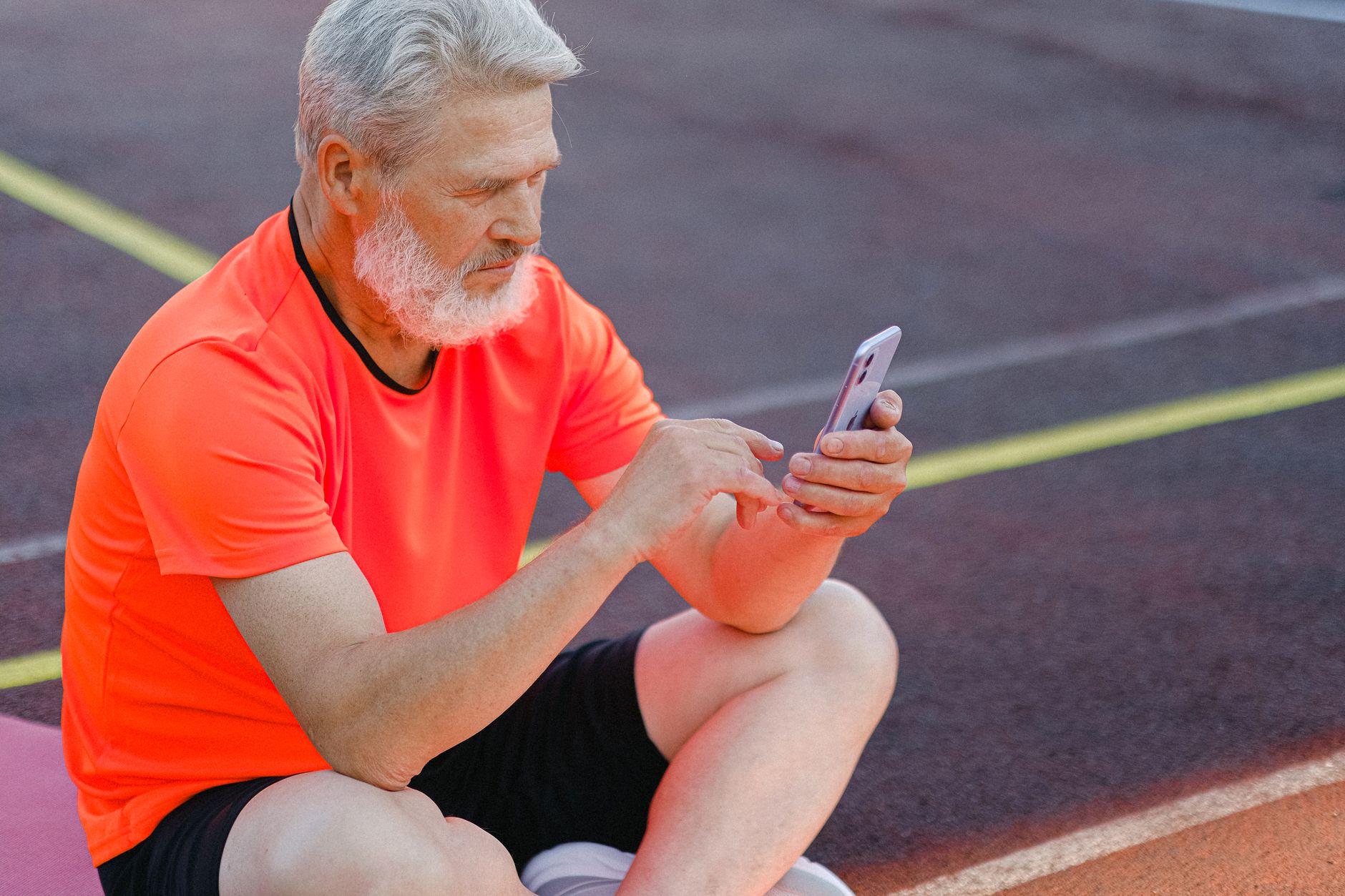 경기도 어르신 스마트폰 무료 교육 5 Senior male athlete in sportswear sitting on sports ground and browsing mobile phone while resting after training