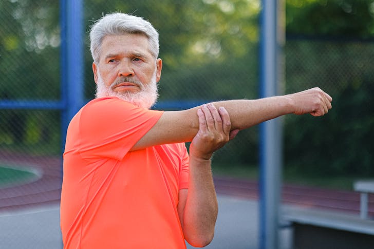 Stylish mature male athlete with modern hairstyle and beard in sportswear stretching before training on stadium