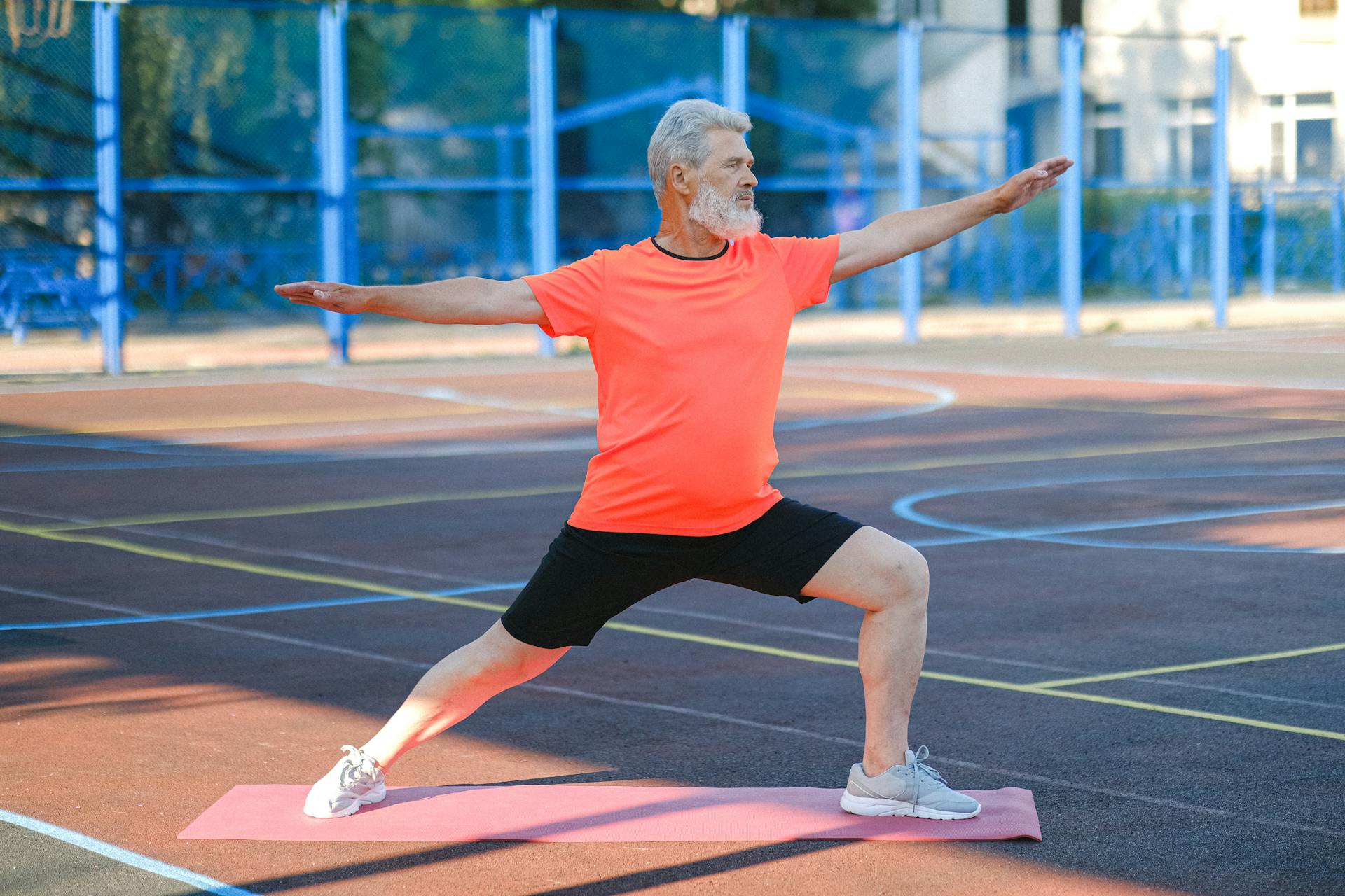 Äldre man i orange skjorta och svarta byxor gör yoga