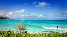 在蔚蓝的天空下，墨西哥坎昆的海滩充满活力，海水碧绿，绿叶葱茏