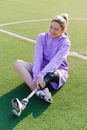 Disabled sportswoman in sneakers with leg prosthesis sitting on green sports ground and laughing