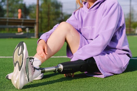 Crop anonymous female athlete with leg prosthesis resting on rubber track in sunny weather