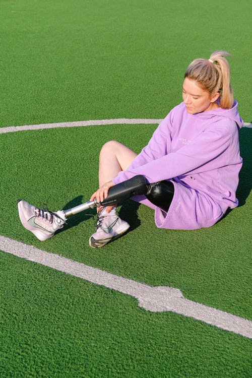 Free Full body of charming female athlete with artificial limb in sportswear resting on stadium during training Stock Photo