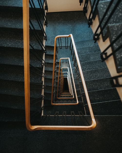 Free A high-angle view of an architectural spiral staircase with black steps and wooden handrails. Stock Photo