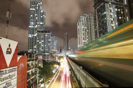Dynamic long exposure shot of Bangkok's skyline with light trails from a skytrain at night.